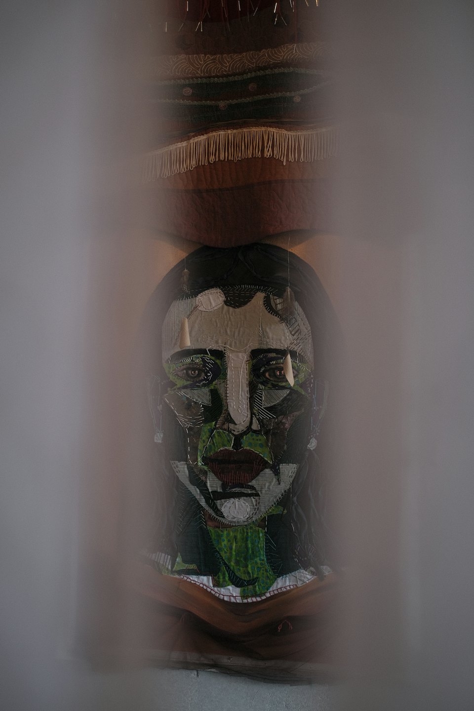 Textilkunst-Gesicht mit grünen, roten und weißen Stoffteilen.